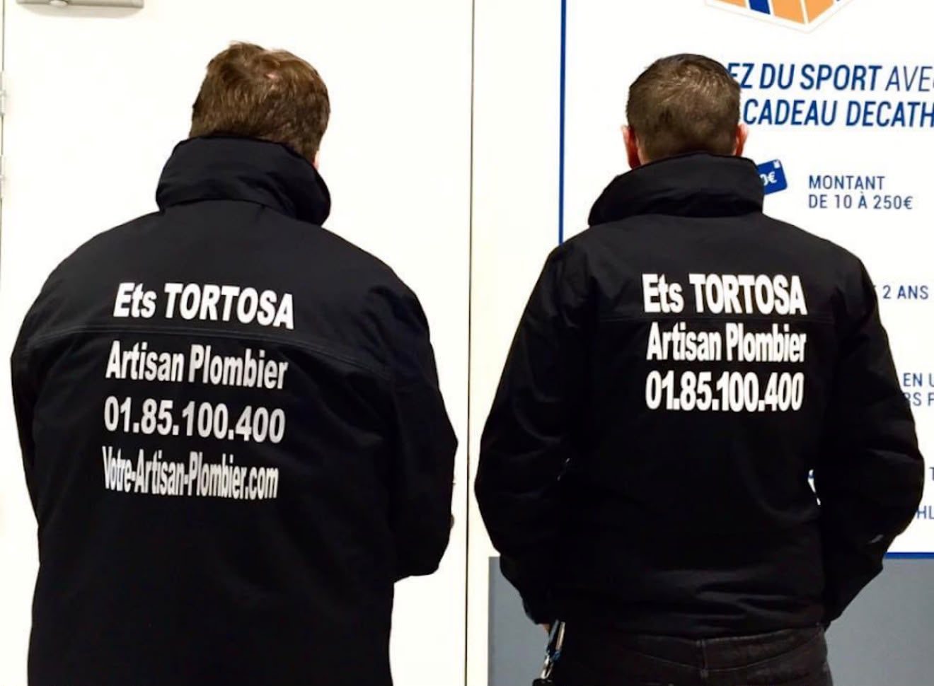Deux plombiers des Ets TORTOSA de dos, vestes floquées Artisan Plombier 01 85 100 400